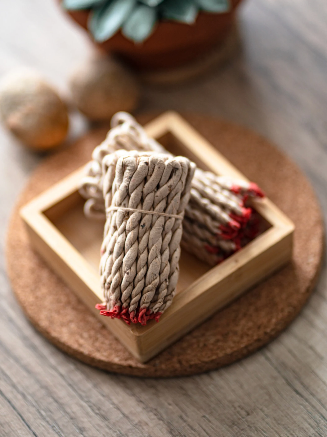 Two braided rope incense bundles with red tips on a wooden coaster.
