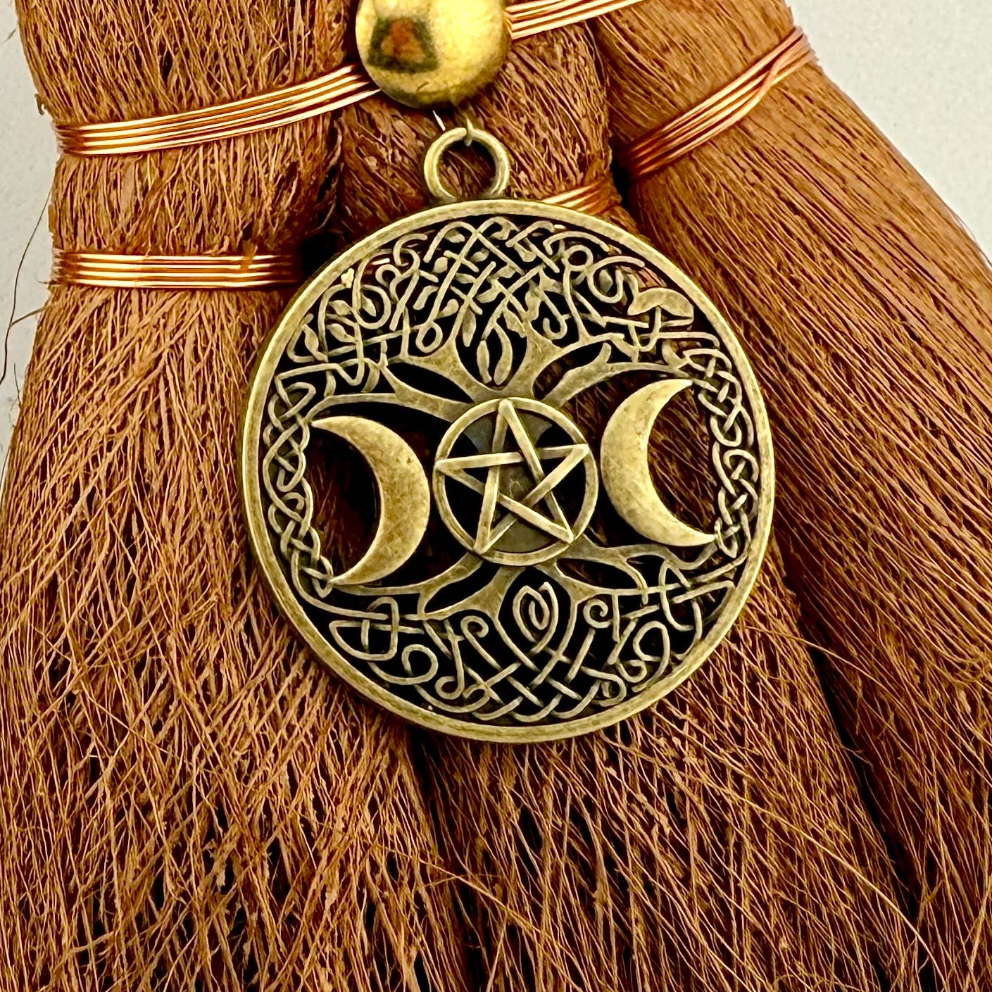 Decorative broom with a gold pendant featuring a pentagram and crescent moons on a white background