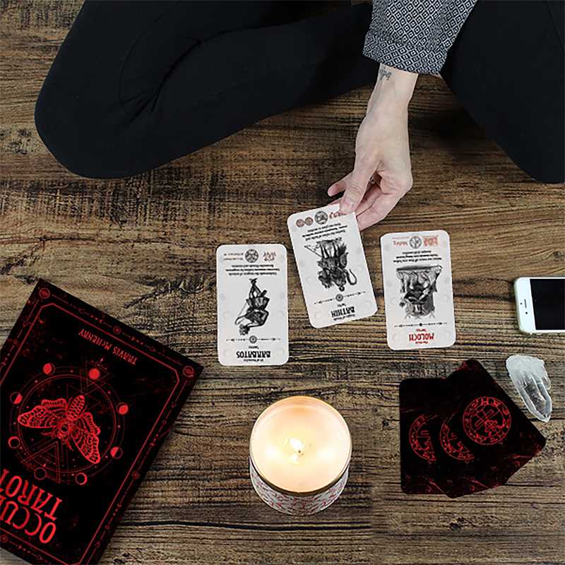 Person playing cards on a wooden table with a candle and phone.