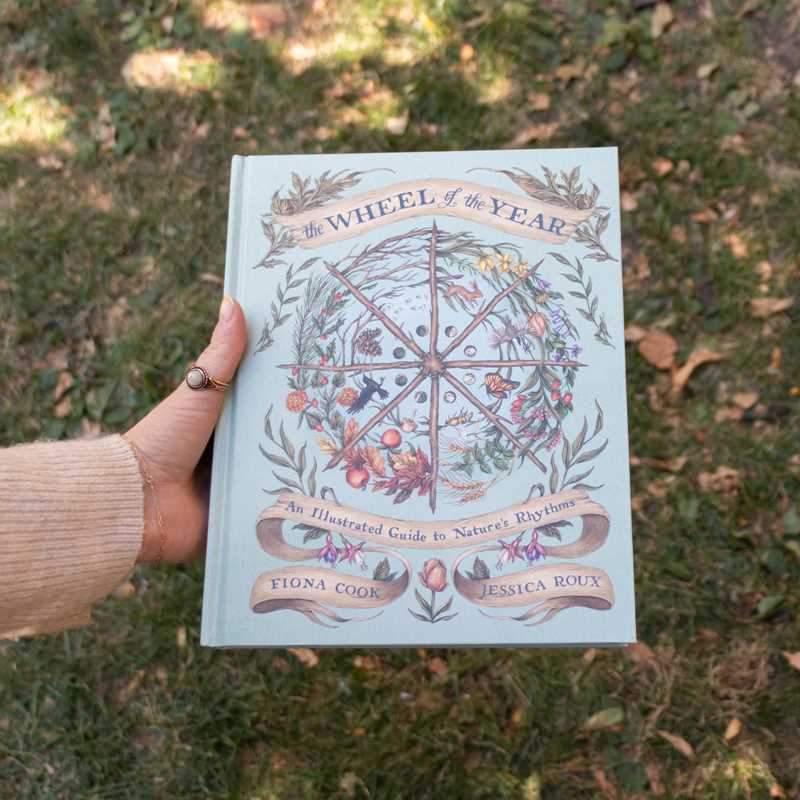 Book titled 'The Wheel of the Year' held in a hand against a grassy background