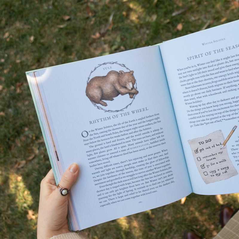 Open book with a bear illustration and text held by a hand against a grassy background