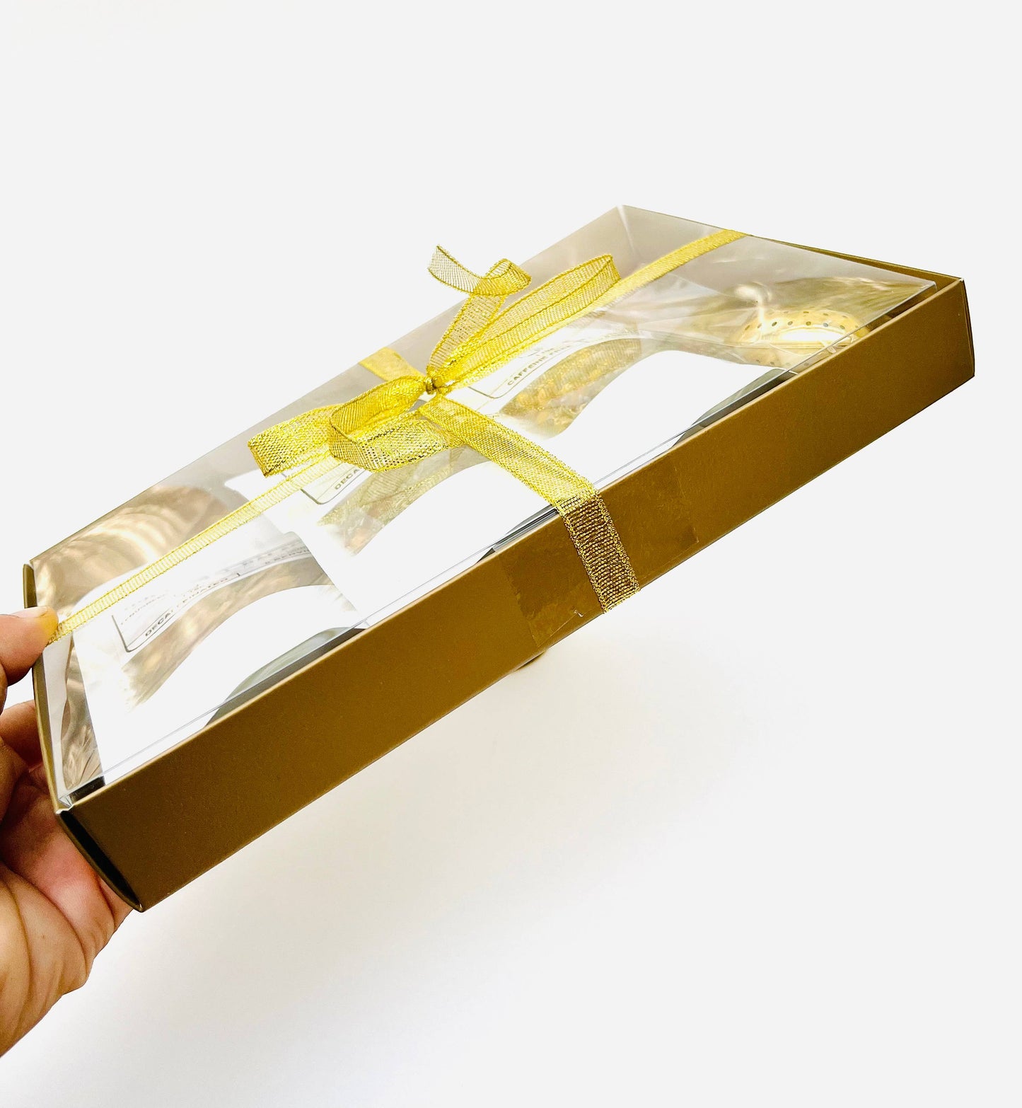 Gold gift box with clear window and yellow ribbon held by a hand on a white background