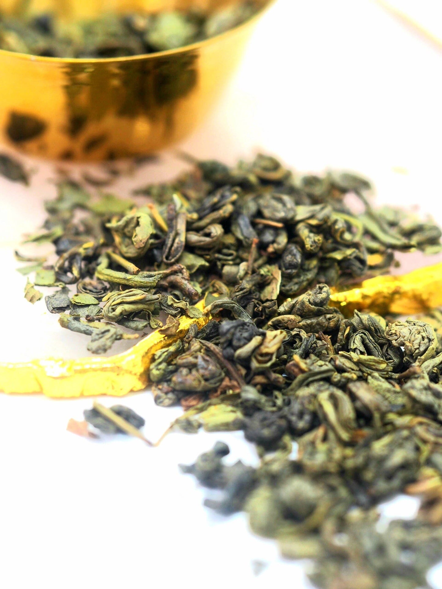 Dry green tea leaves with a gold teacup in the background