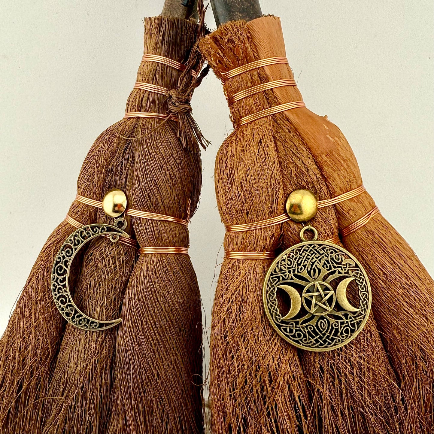 Two broomsticks with decorative charms on a neutral background