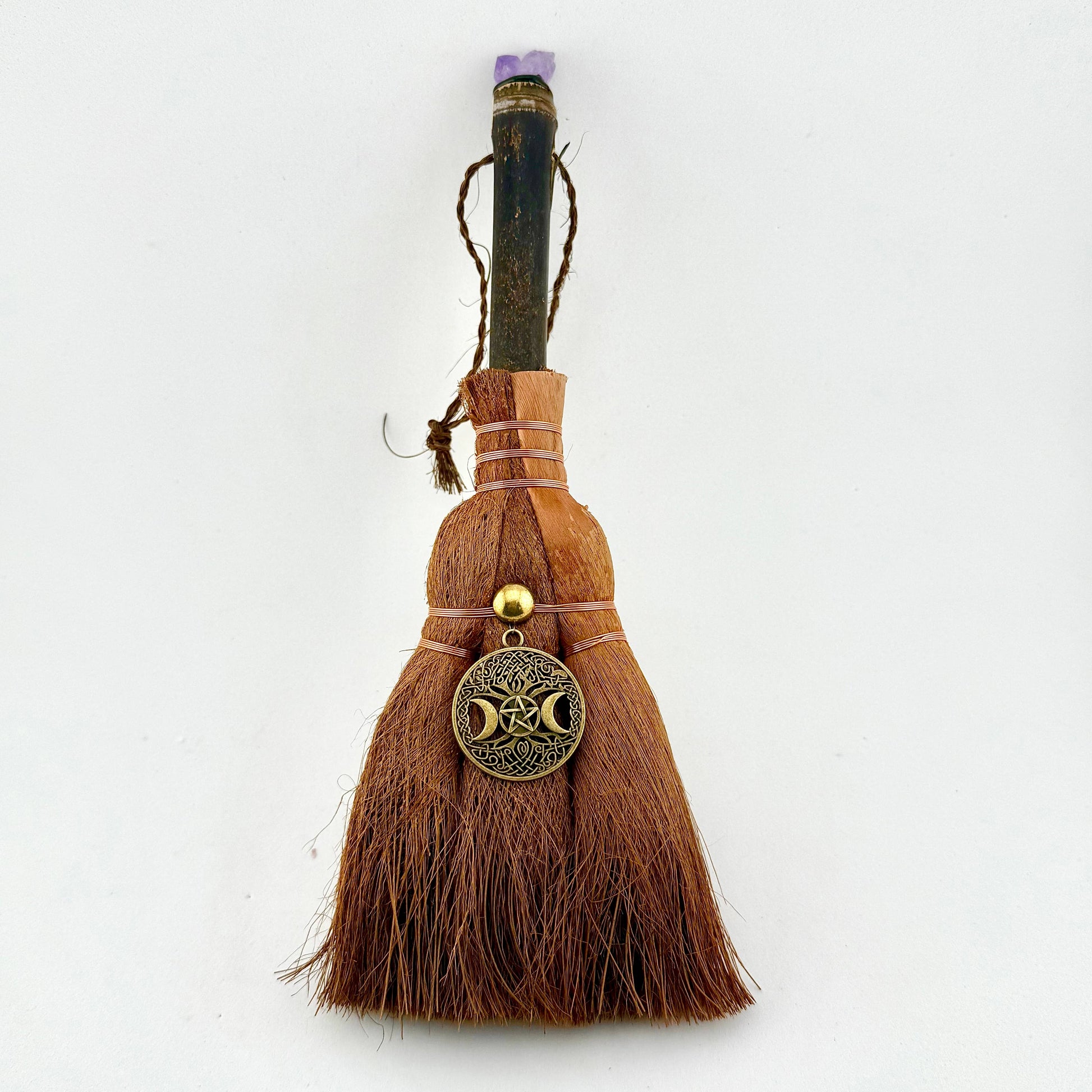 Witch's broom with a brass Crescent Moon Charm on a white background