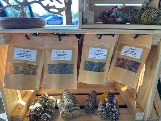 Ritual Herbs packages and smudge sticks on a wooden shelf.