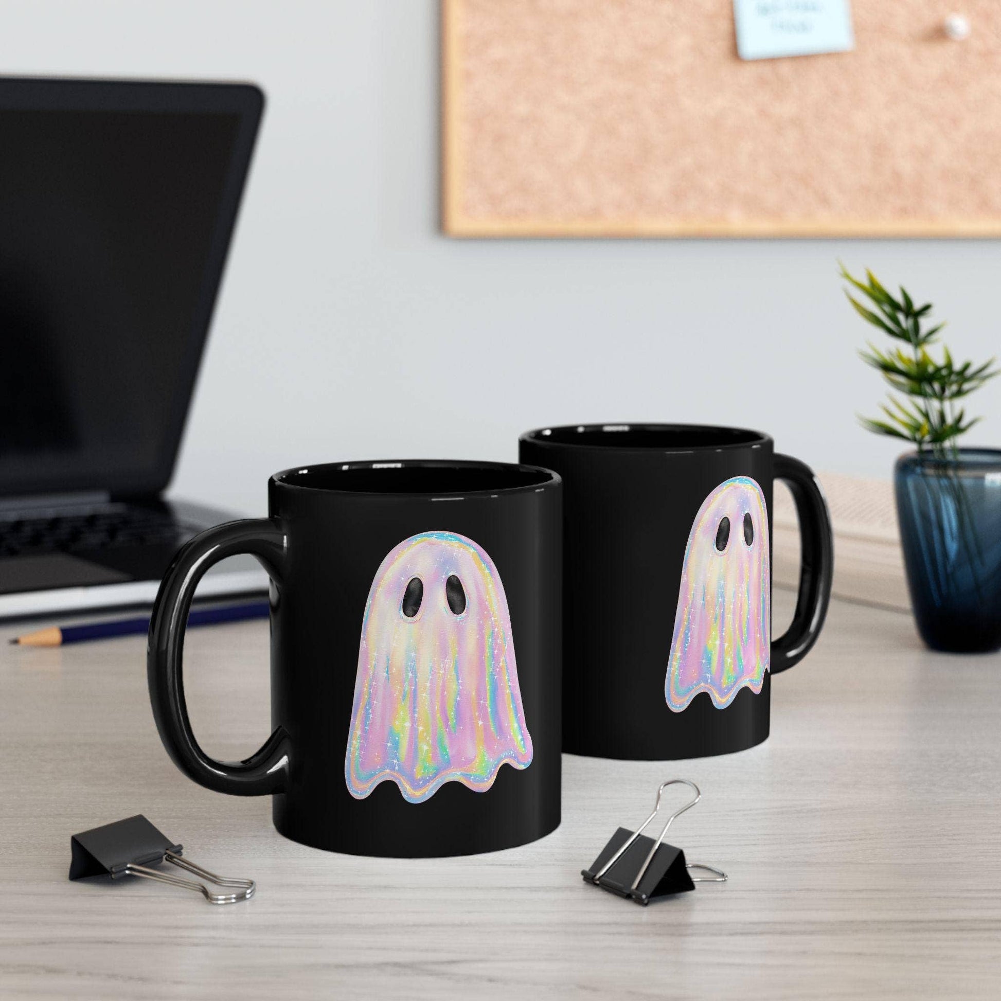 Two black mugs with ghost designs on a desk with office supplies.