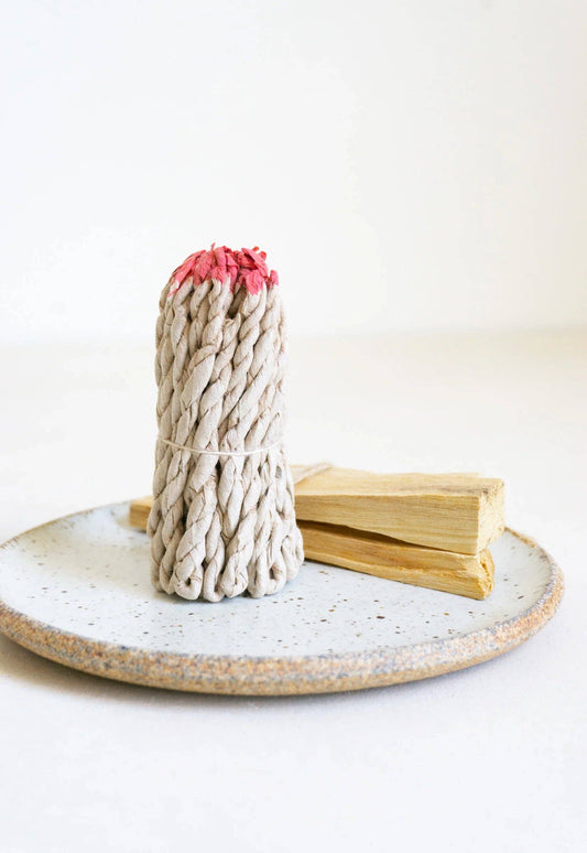 rope incense with red tips on a ceramic plate against a white background