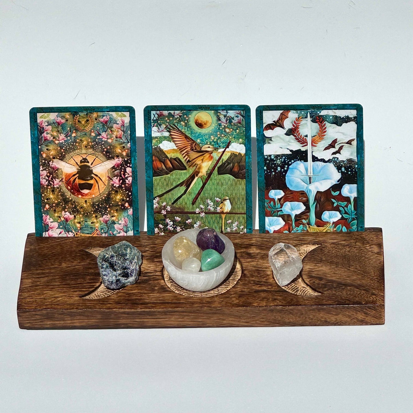 Three tarot cards on a wooden stand with crystals and stones below against a white background
