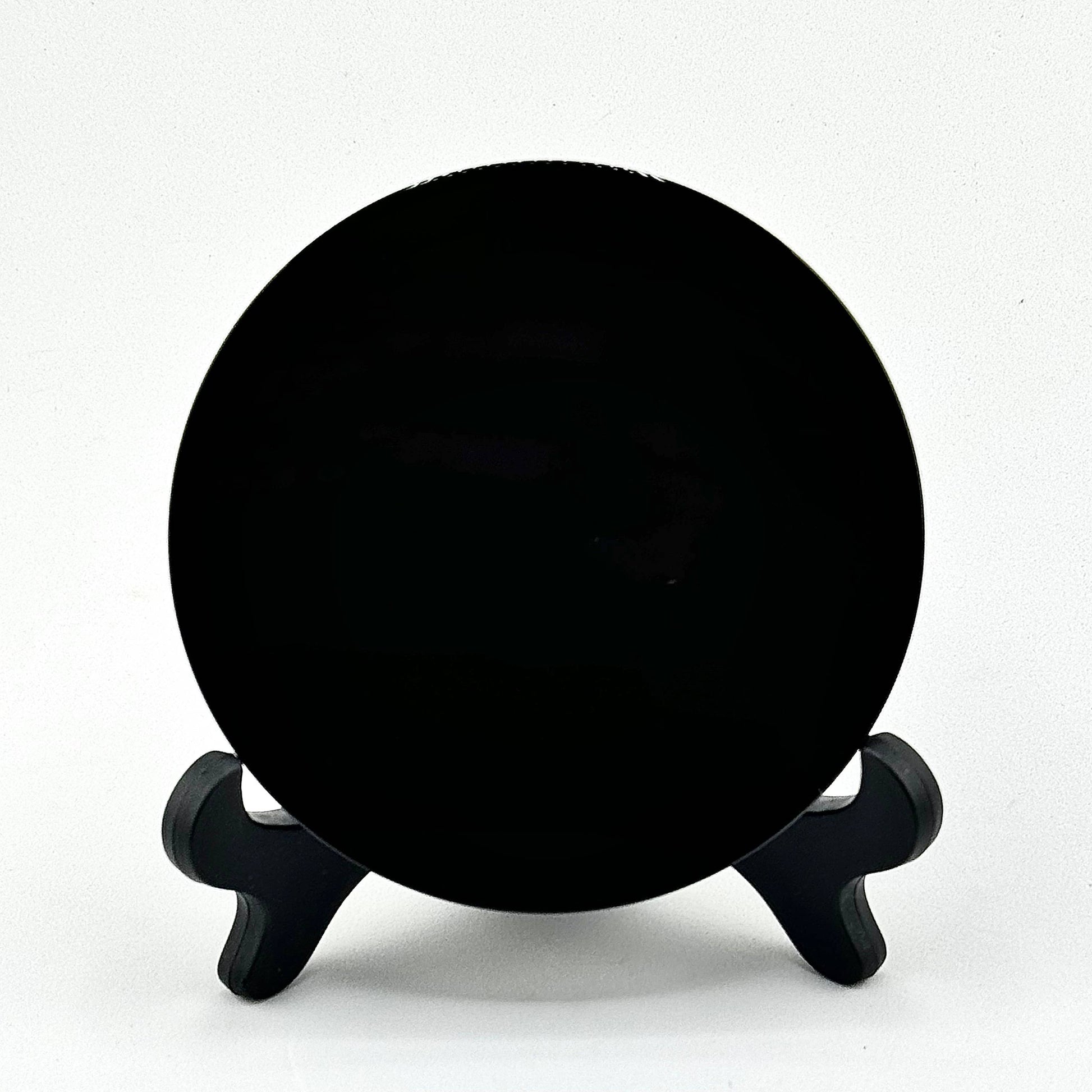 Black scrying mirror on a stand against a white background