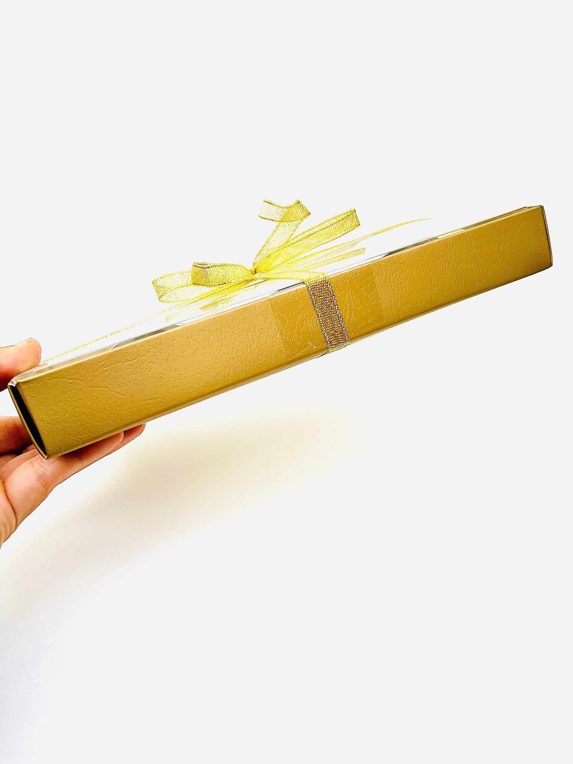 Gold gift box with a yellow ribbon held by a hand on a white background