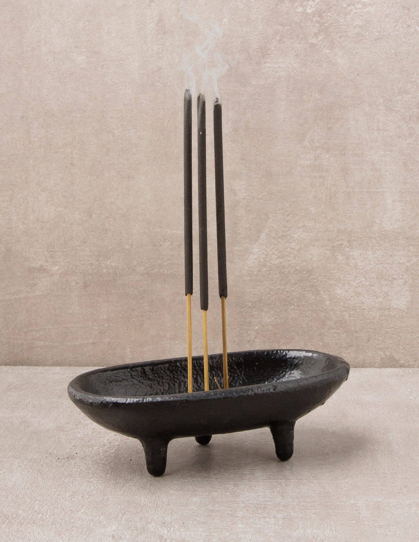 Black incense holder with three incense sticks on a neutral background