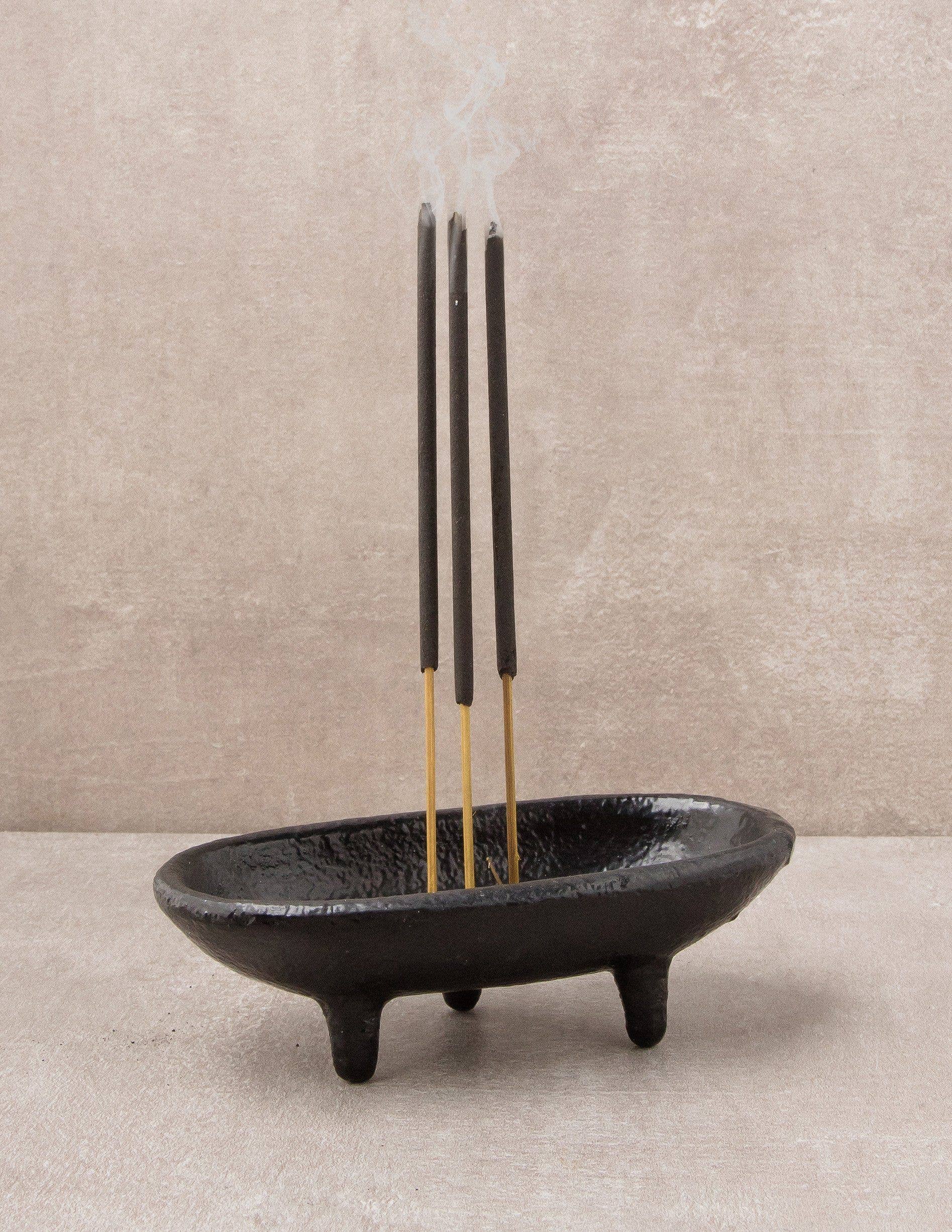 Black incense holder with three incense sticks on a neutral background