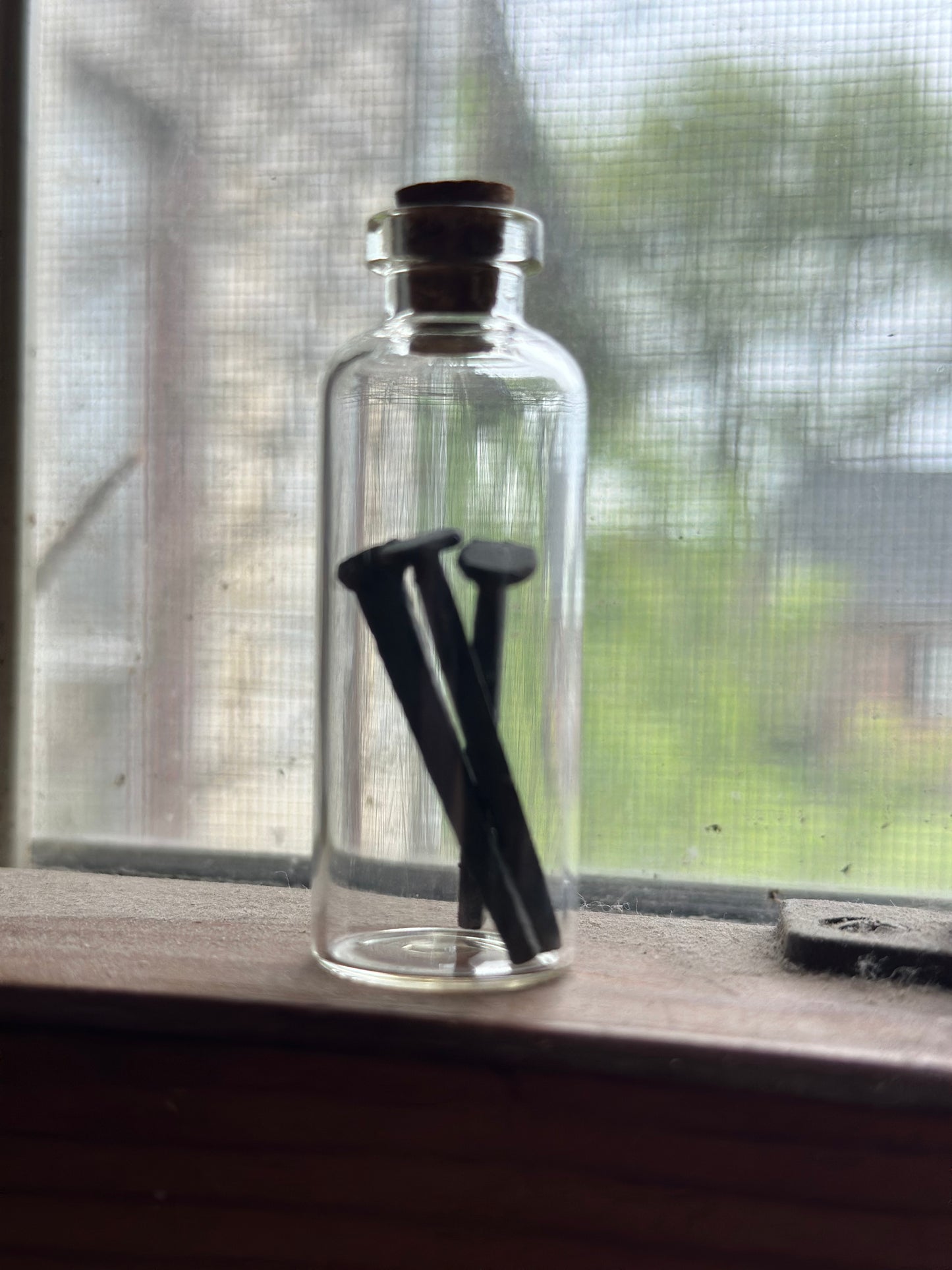 Clear glass bottle with vintage forged iron nails inside on a windowsill