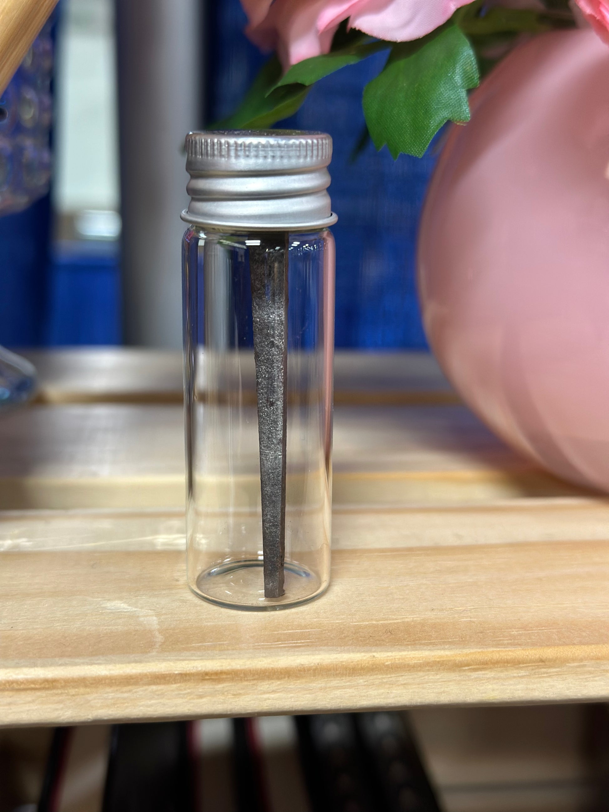 Clear glass bottle with silver cap on a wooden surface, with vintage forged iron nails